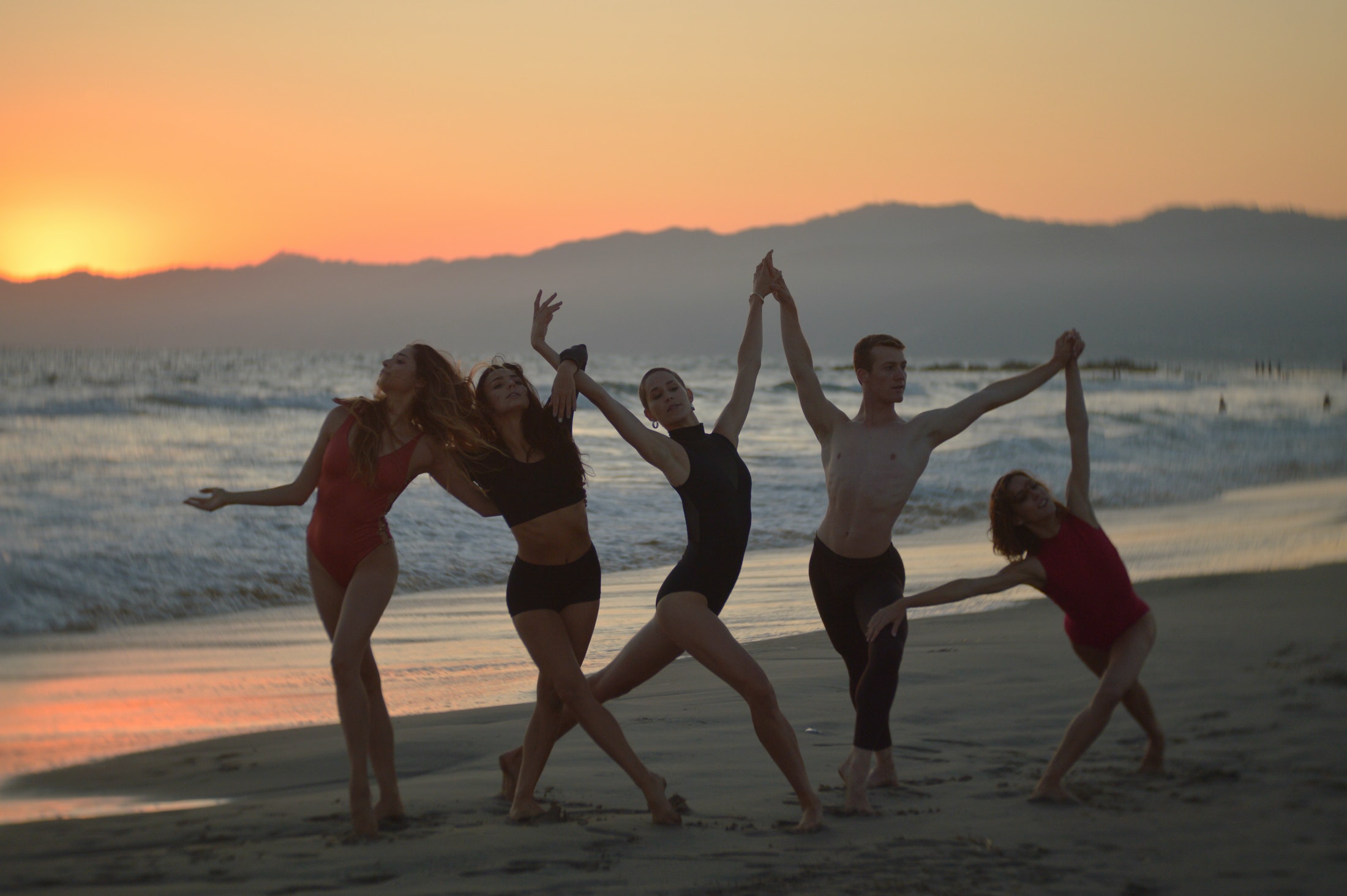 Joyful slim friends dancing on sandy seashore at sundown
